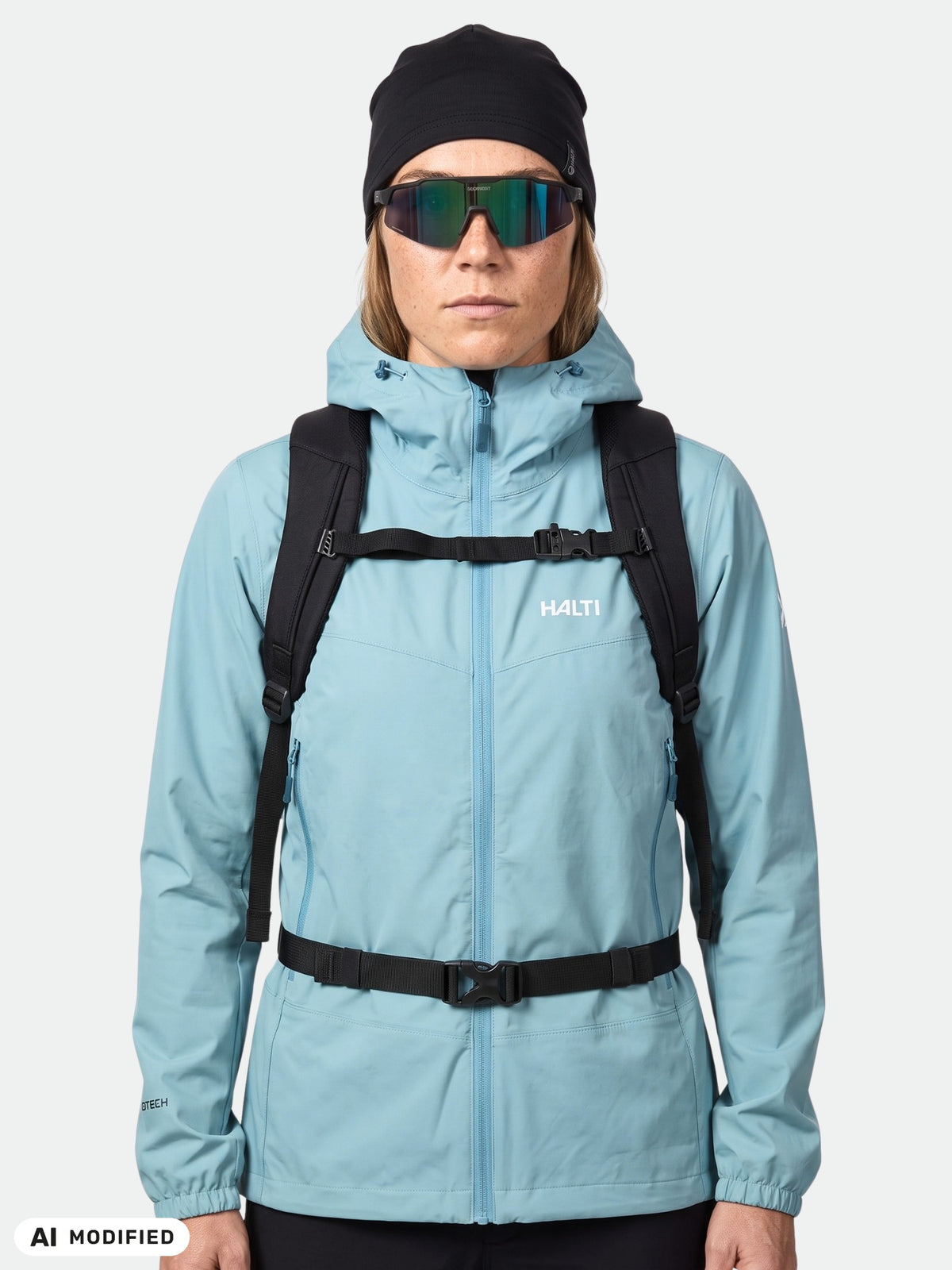 Woman in Halti Pallas Evo X-stretch jacket, black hat, sunglasses, and backpack facing forward.