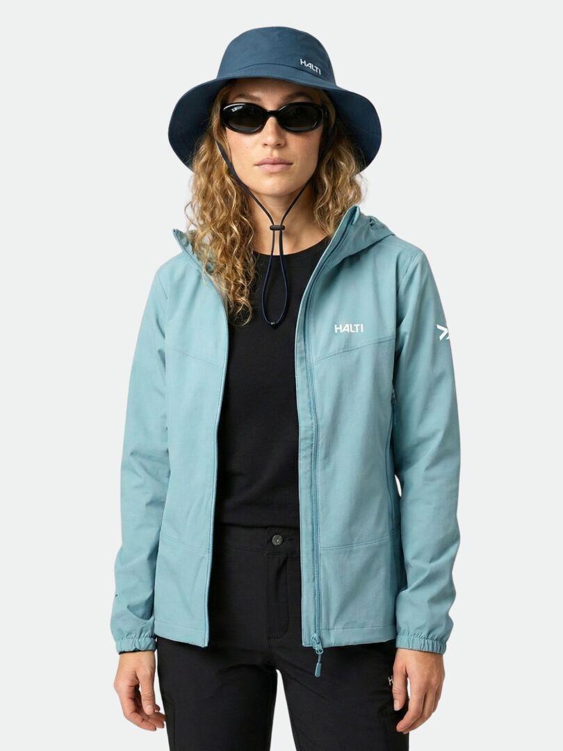 A woman wears the Halti Pallas Evo X-stretch Jacket in blue, with a black shirt, pants, blue hat, and sunglasses.