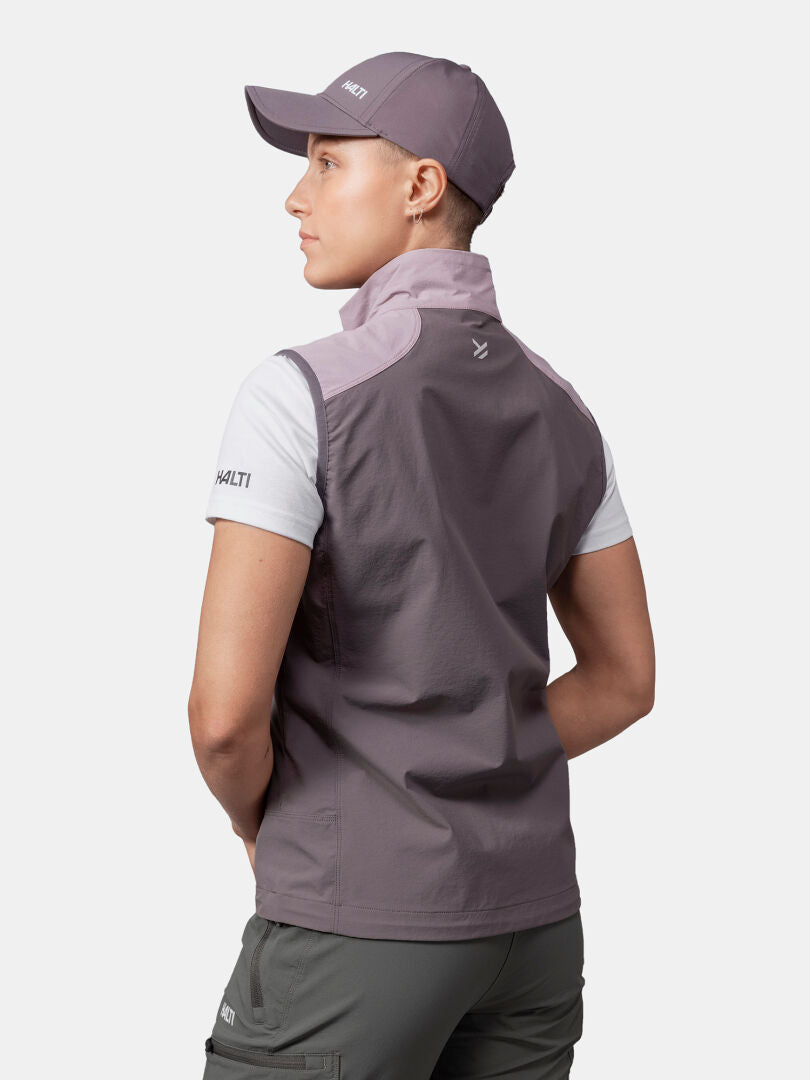 Person facing away in Halti Pallas Evo X-stretch Vest Women's, white shirt, gray cap, green pants on white background.