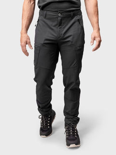 A man wears Halti Pallas Evo Brushed X-stretch Pants with hiking boots, standing against a light gray background.