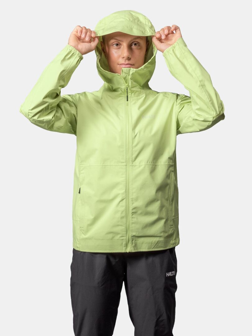 A person wears the Halti Pisarat 2,5L DX Shell Jacket Women's in light green, holding the hood with both hands.
