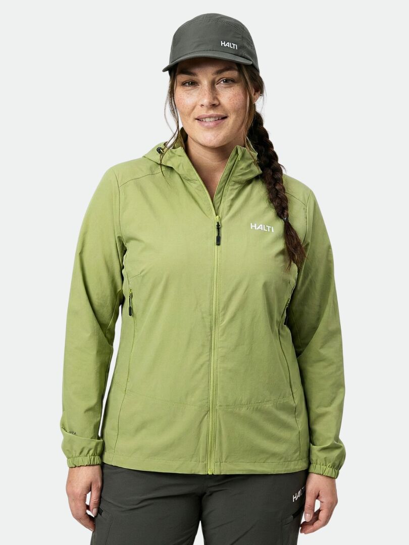 Woman wearing a Halti Pallas Evo X-stretch Jacket Plus in light green, dark green pants, and matching cap, facing forward.