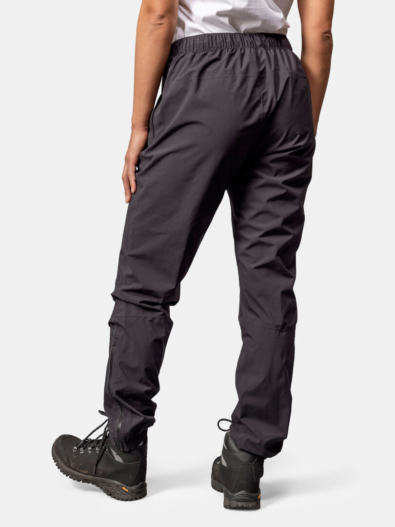 A person wears Halti Pisarat 2.5L DX Shell Pants and black hiking boots, standing with their back to the camera.