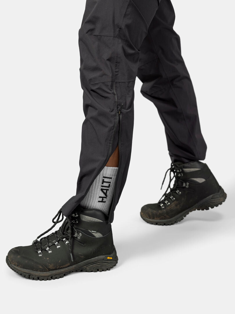 Person in black hiking boots, gray Halti socks, and Halti Pisarat 2.5L DX Shell Pants with ankle zipper partly open.