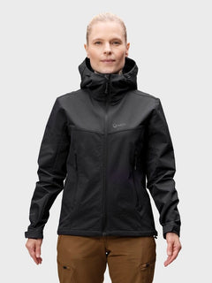 A woman wears the Halti Pallas Evo Brushed X-stretch Jacket, black, paired with brown pants against a light gray background.