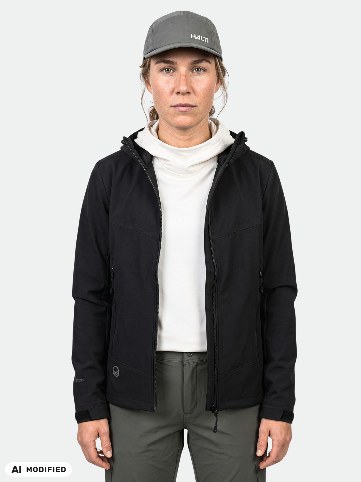 A person in a black Halti Pallas Evo Brushed X-stretch Jacket, white mock-neck top, dark trousers, and a grey baseball cap.