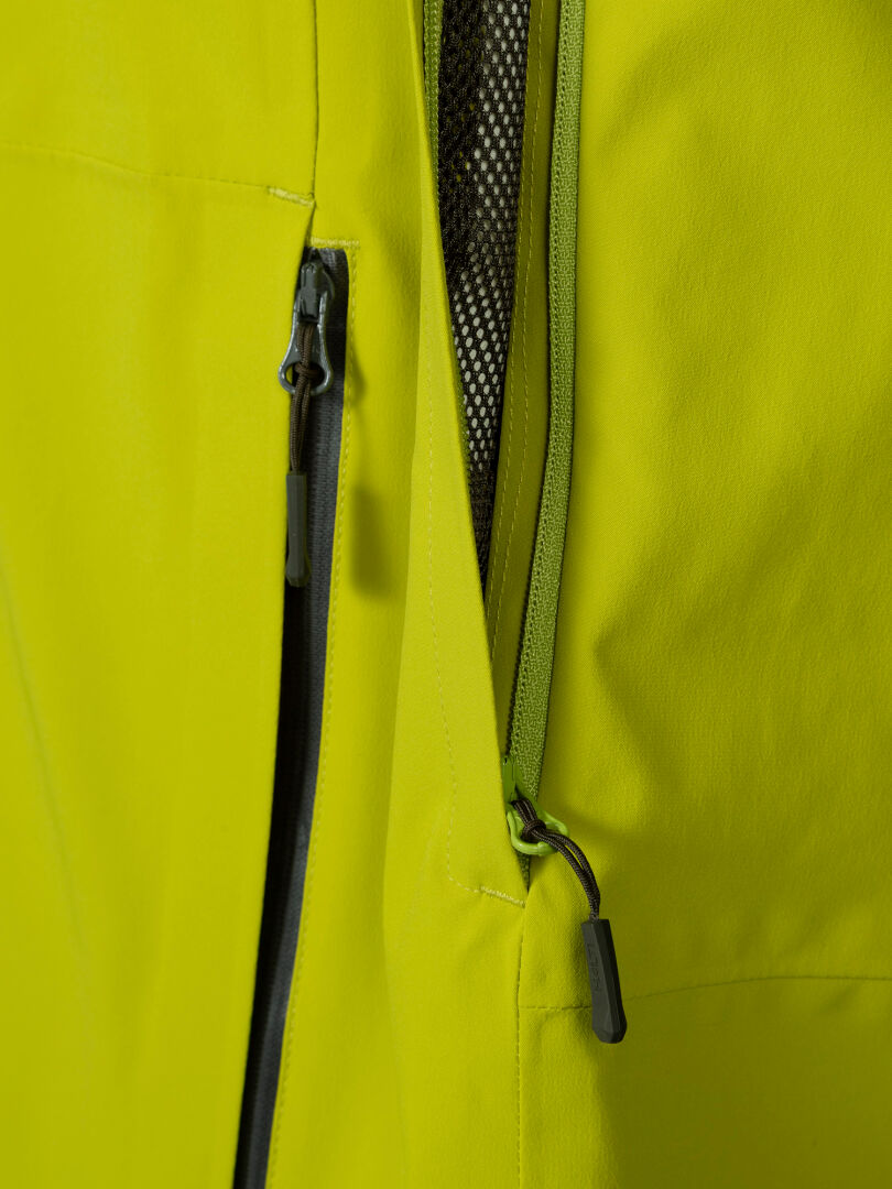 Close-up of Halti’s Staala DX Shell Jacket Men's, featuring a zippered mesh pocket and green zipper pulls.