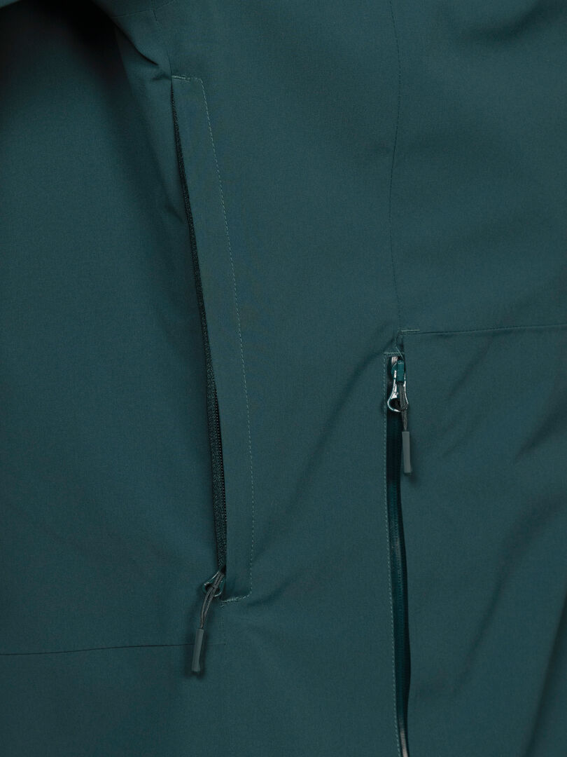 Close-up of Halti Staala DX Shell Jacket Men’s in dark teal, featuring two zippered pockets with black pulls.