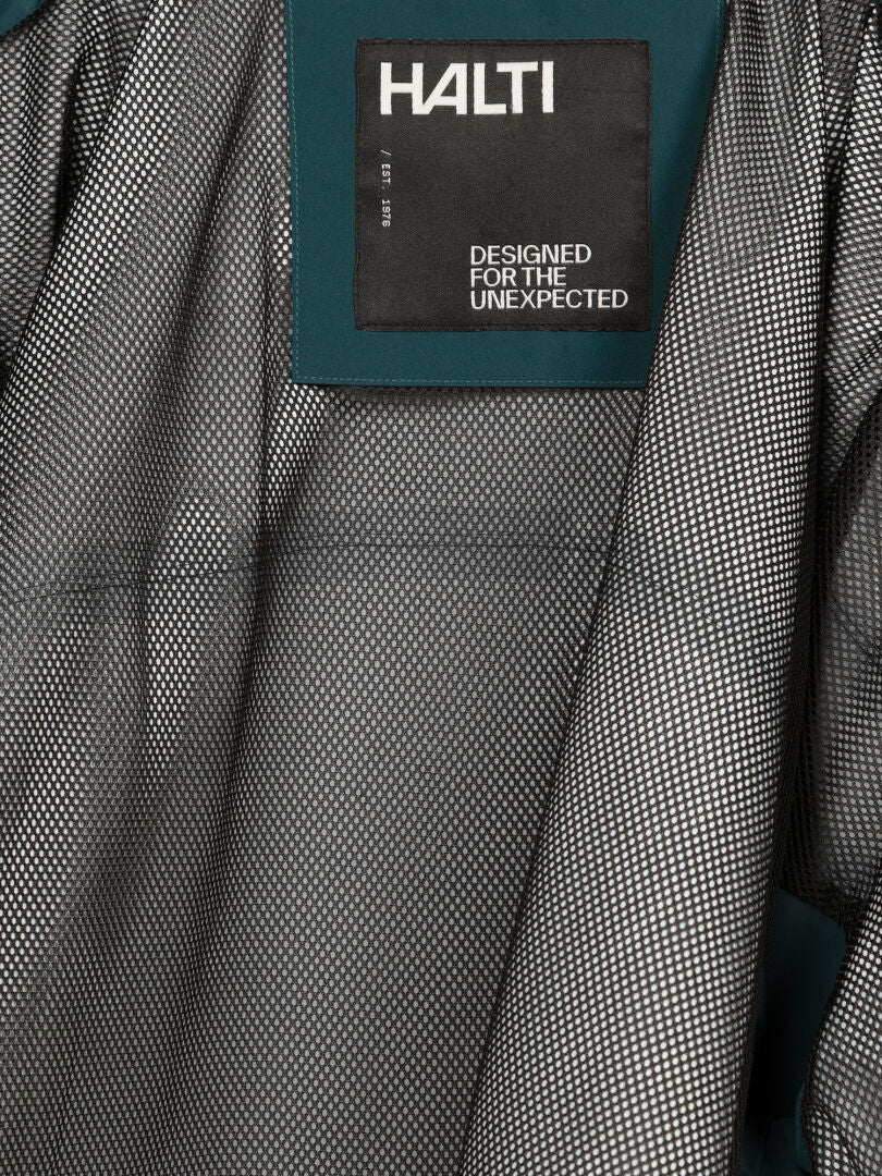 Close-up of a Halti Staala DX Shell Jacket Men’s label: DESIGNED FOR THE UNEXPECTED on textured fabric.