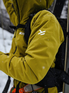Man wearing Halti Staala DrymaxX Shell Jacket stands outdoors in snow, holding ski or hiking gear.