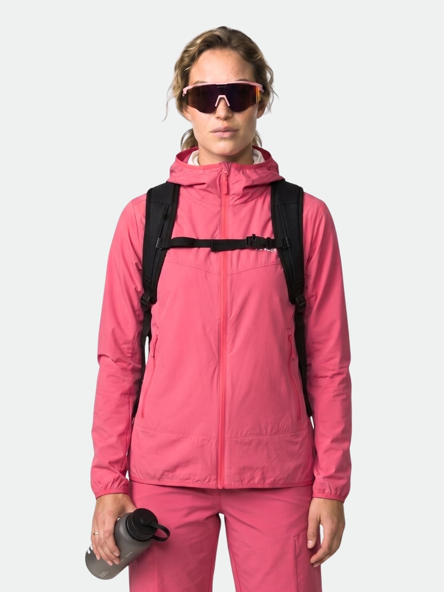 A person in a pink Halti Pallas Cool X-stretch Jacket, pants, black backpack, sunglasses, and gray water bottle.