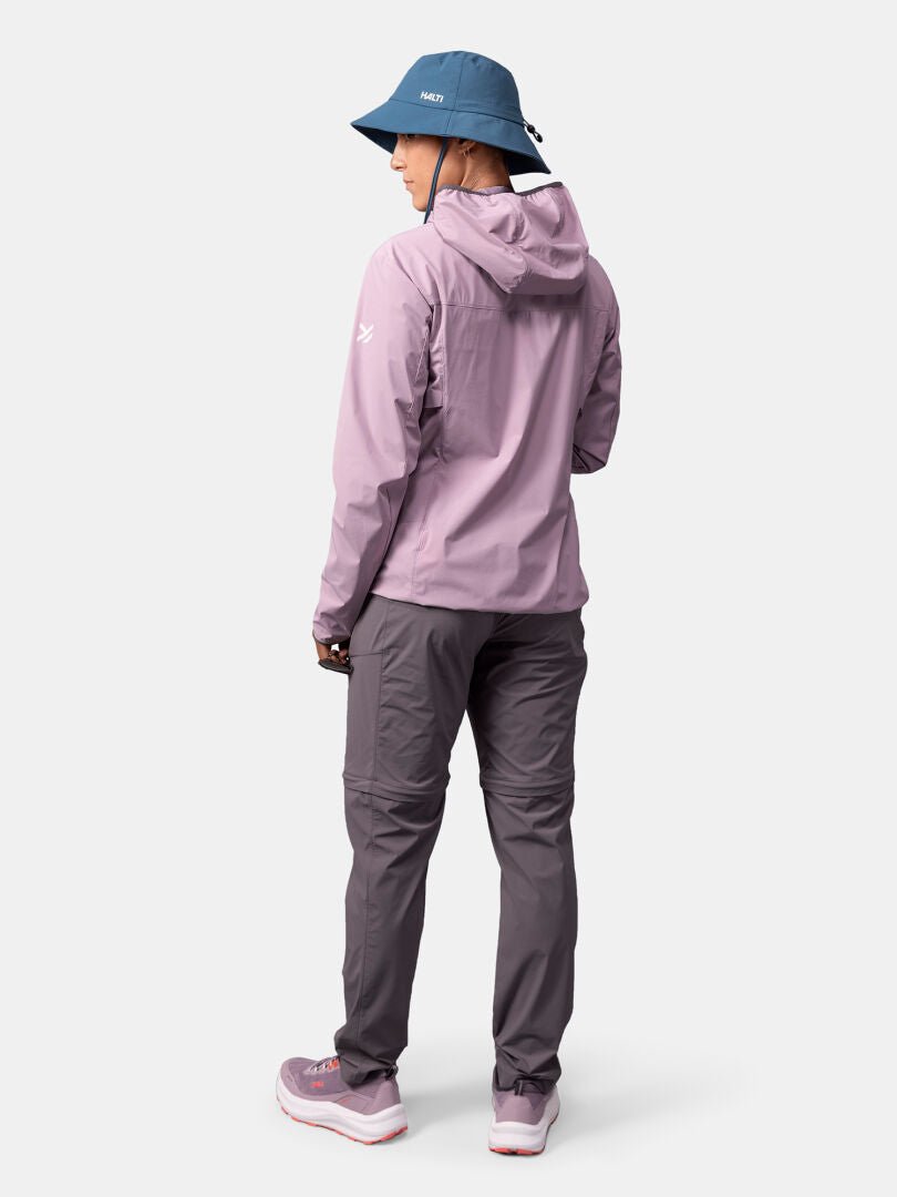 Woman in Halti Pallas Cool X-stretch Jacket, blue hat, and gray pants facing away against a white background.