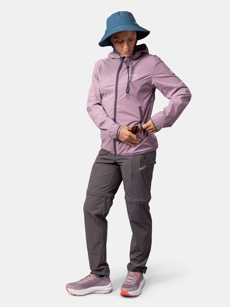 Wearing the Halti Pallas Cool X-stretch Jacket Women's, she adjusts the zipper, styled with gray pants and sneakers.