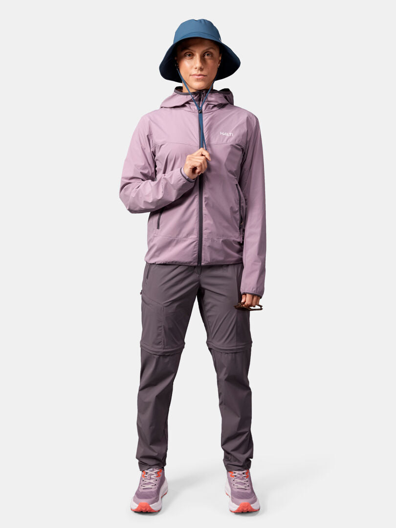 Person wears Halti Pallas Cool X-stretch Jacket in purple, gray pants, blue hat, and sneakers against a plain background.