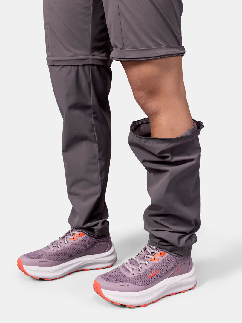 A person wears Halti Pallas Cool Stretch Zip-off Pants with one leg zipped off, showing shorts and purple sneakers.