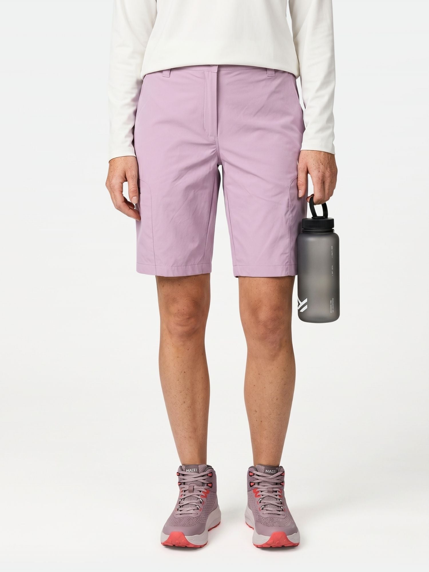 A person in Halti Pallas Cool Shorts for women, a white long-sleeve top, pink sneakers, and holding a water bottle.