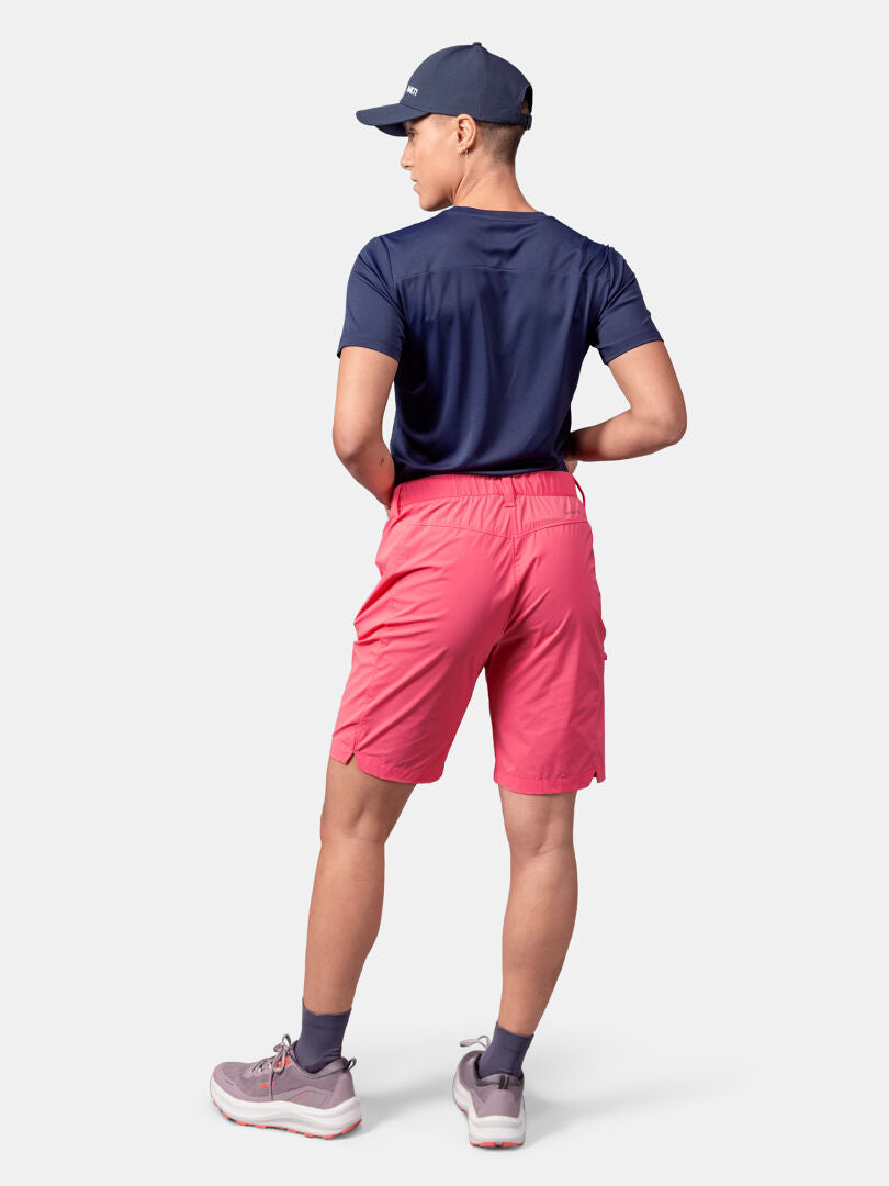 Person standing and facing away, wearing a navy cap, navy shirt, Halti Pallas Cool Shorts Women's (pink), gray socks, gray sneakers.