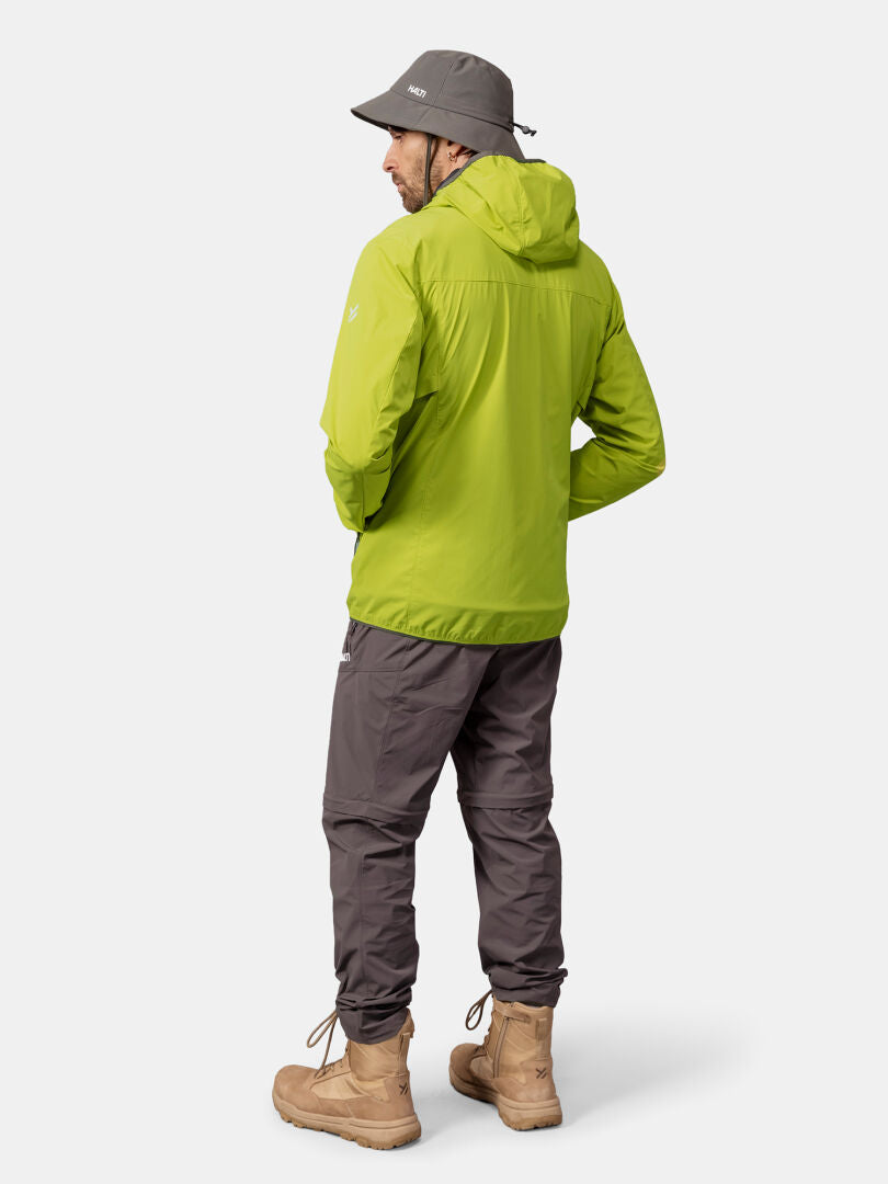 A person in a green Halti Pallas Cool X-stretch Jacket, gray pants, tan boots, and a gray bucket hat stands facing away.
