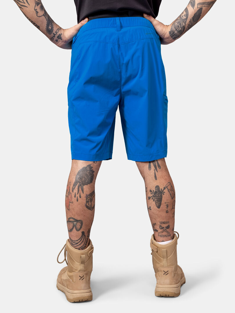 Man seen from the back wears Halti Pallas Cool X-stretch Shorts, tan boots, with tattoos on arms and legs visible.