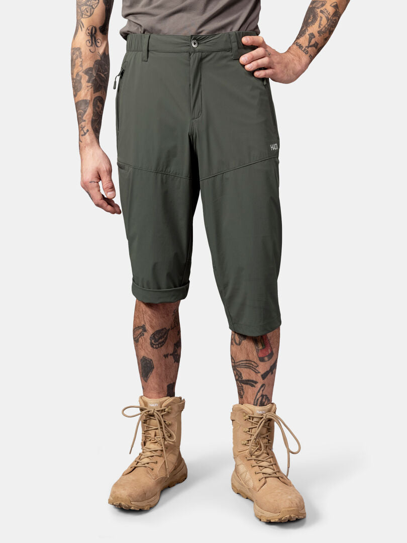 A person in Halti Pallas Cool X-stretch Capri Pants, a gray shirt, and tan boots stands against a plain background.