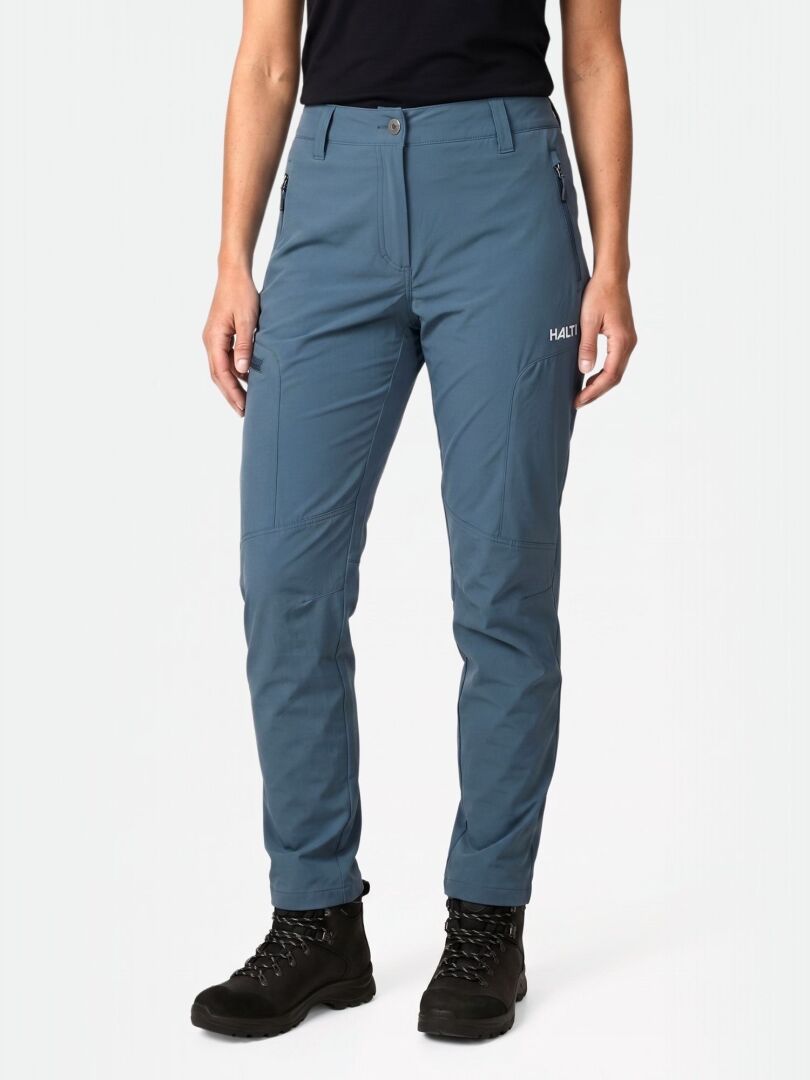 A woman in Halti Pallas Cool X-stretch Pants and black boots stands against a plain light background.