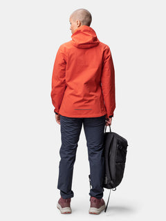 Woman facing away in a red Halti Finholma X-stretch Jacket, dark pants, holding a black backpack by her side.
