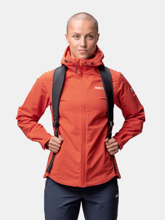A woman wears the Halti Finholma X-stretch Jacket in orange with a black backpack, standing against a white background.