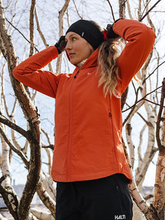 A woman in a Halti Finholma X-stretch Jacket adjusts her hair outdoors near leafless trees.