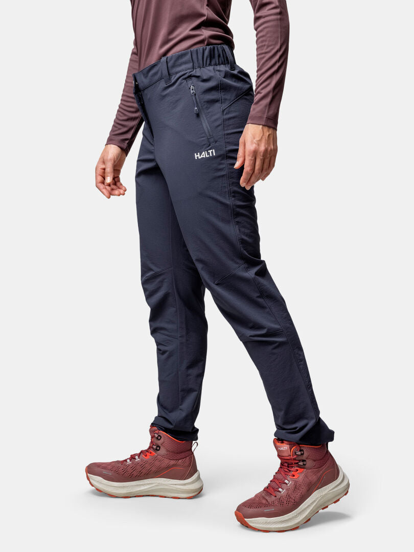 A woman in Halti Finholma X-stretch Pants, a long-sleeve shirt, and red hiking boots stands against a plain background.