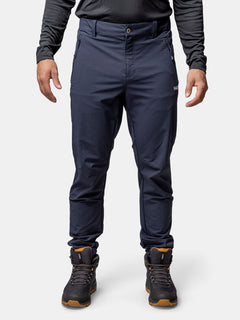 A person in Halti Finholma X-stretch Pants, black long-sleeve top, and hiking boots with brown soles stands upright.