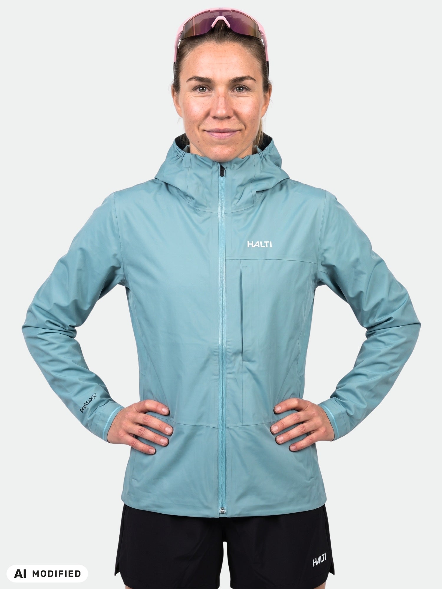 Woman in Halti Taival DX 3L light blue hooded jacket, black shorts, sunglasses on head, standing hands on hips.