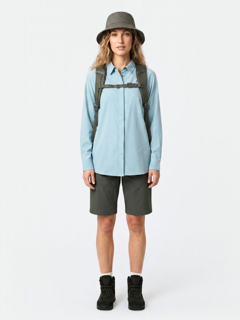 Woman faces forward in wide-brim hat, Halti Samoy Longsleeve Trekking Shirt, backpack, dark shorts, and hiking boots.