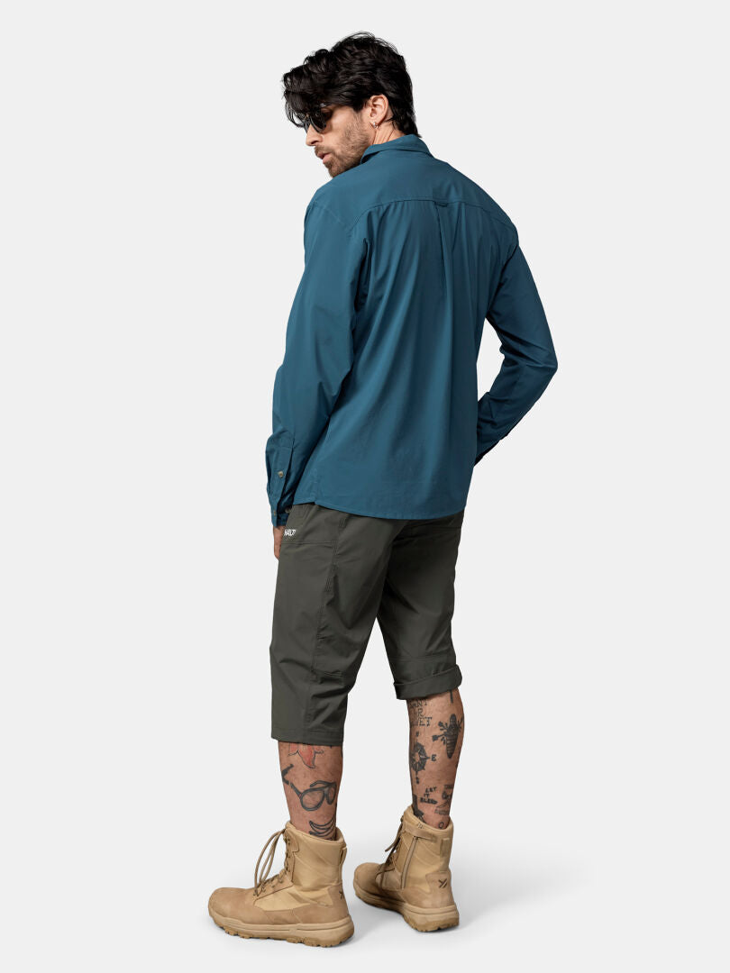 Man in Halti Samoy Longsleeve Trekking Shirt, olive shorts, tan boots, and leg tattoos stands facing away.