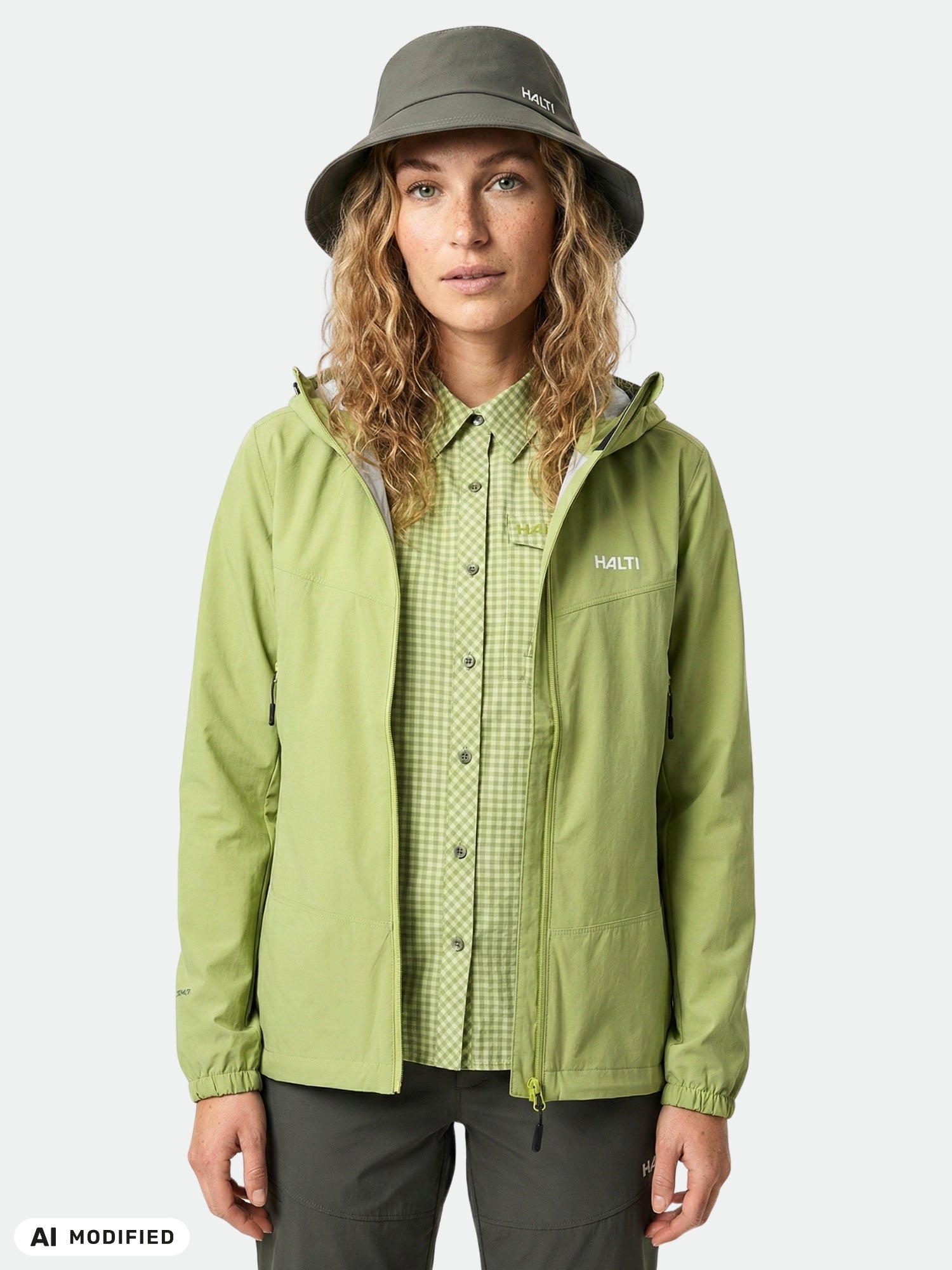 Woman in Halti Pallas Evo X-stretch Jacket, green check shirt, and gray hat stands against a plain background.