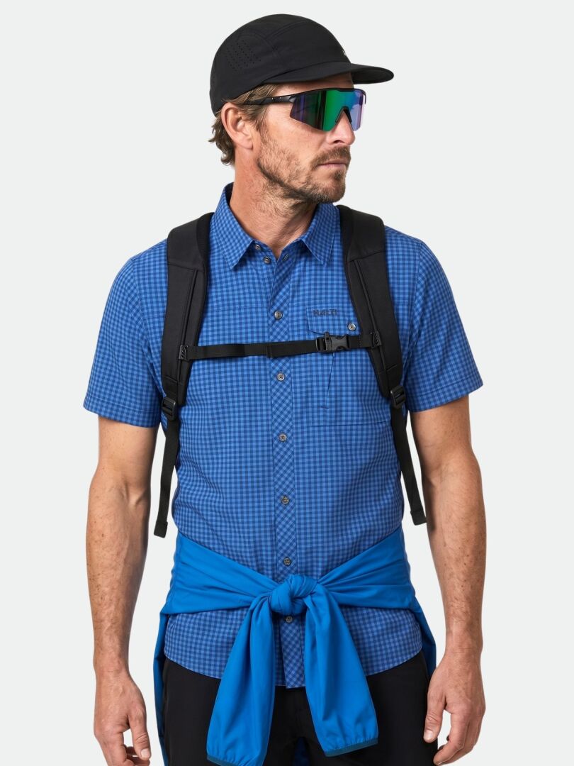 A man in a blue Halti Samoy Trekking Shirt, backpack, sunglasses, cap, and a blue jacket tied at his waist.