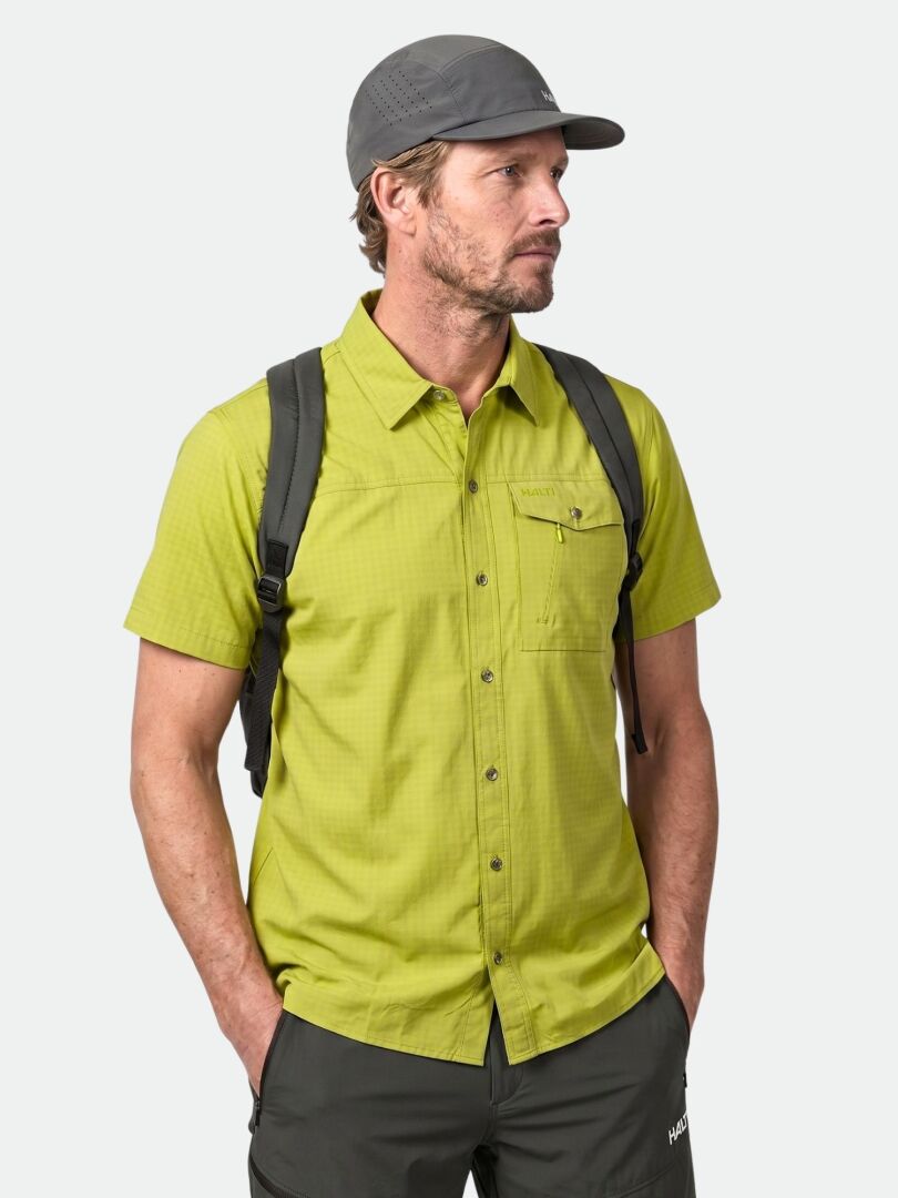 Man in Halti Samoy Trekking Shirt, gray cap, backpack, dark pants—hands in pockets outdoors.