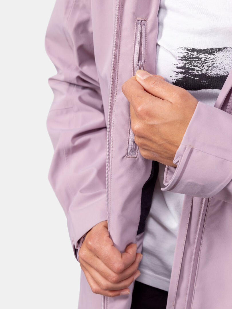 A woman in a Halti Valaja DX Parka Jacket unzips a vertical chest pocket, showing part of a white shirt underneath.