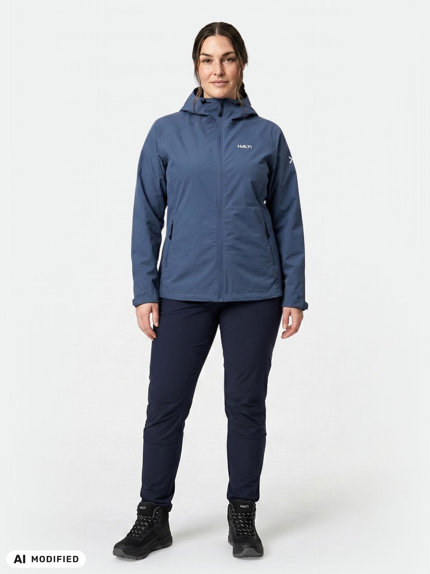A woman stands forward in the Halti Finholma X-stretch Jacket Women's Plus, dark pants, and black hiking boots.