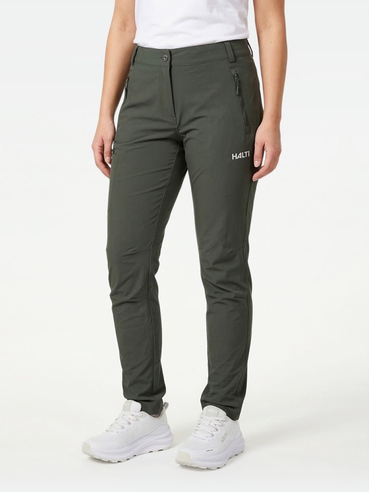 A woman in Halti Pallas X-stretch Outdoor Pants, a white shirt, and white sneakers stands against a plain background.