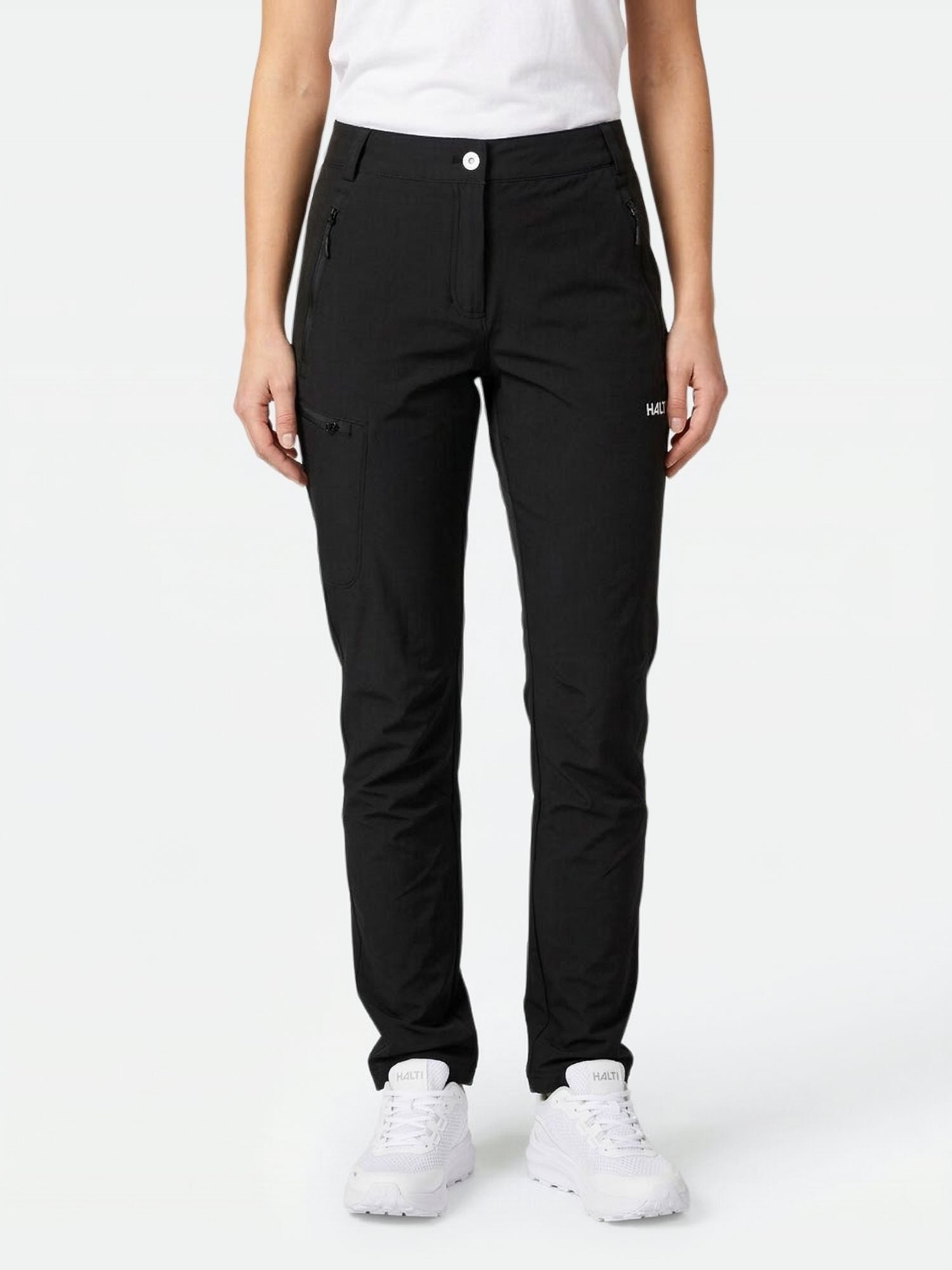A woman wears Halti Pallas X-stretch Outdoor Pants, a white T-shirt, and white sneakers against a plain background.