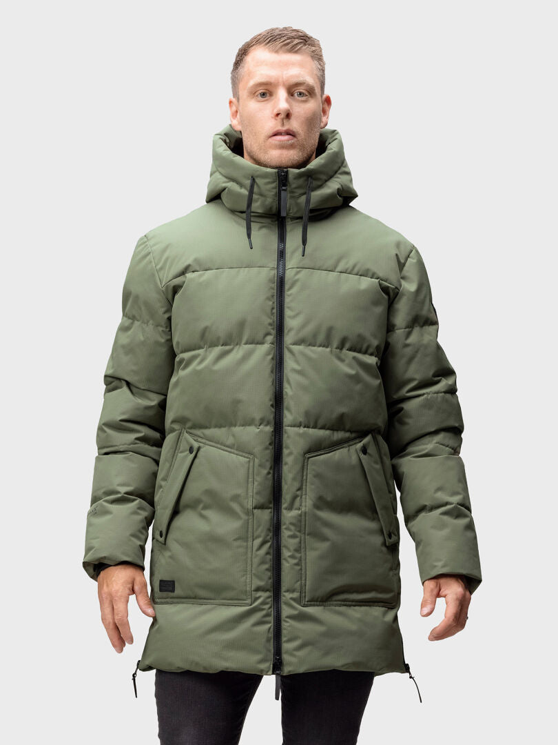 A man wears the Halti Linjat Parka Jacket in olive green with a hood, standing against a light gray background.