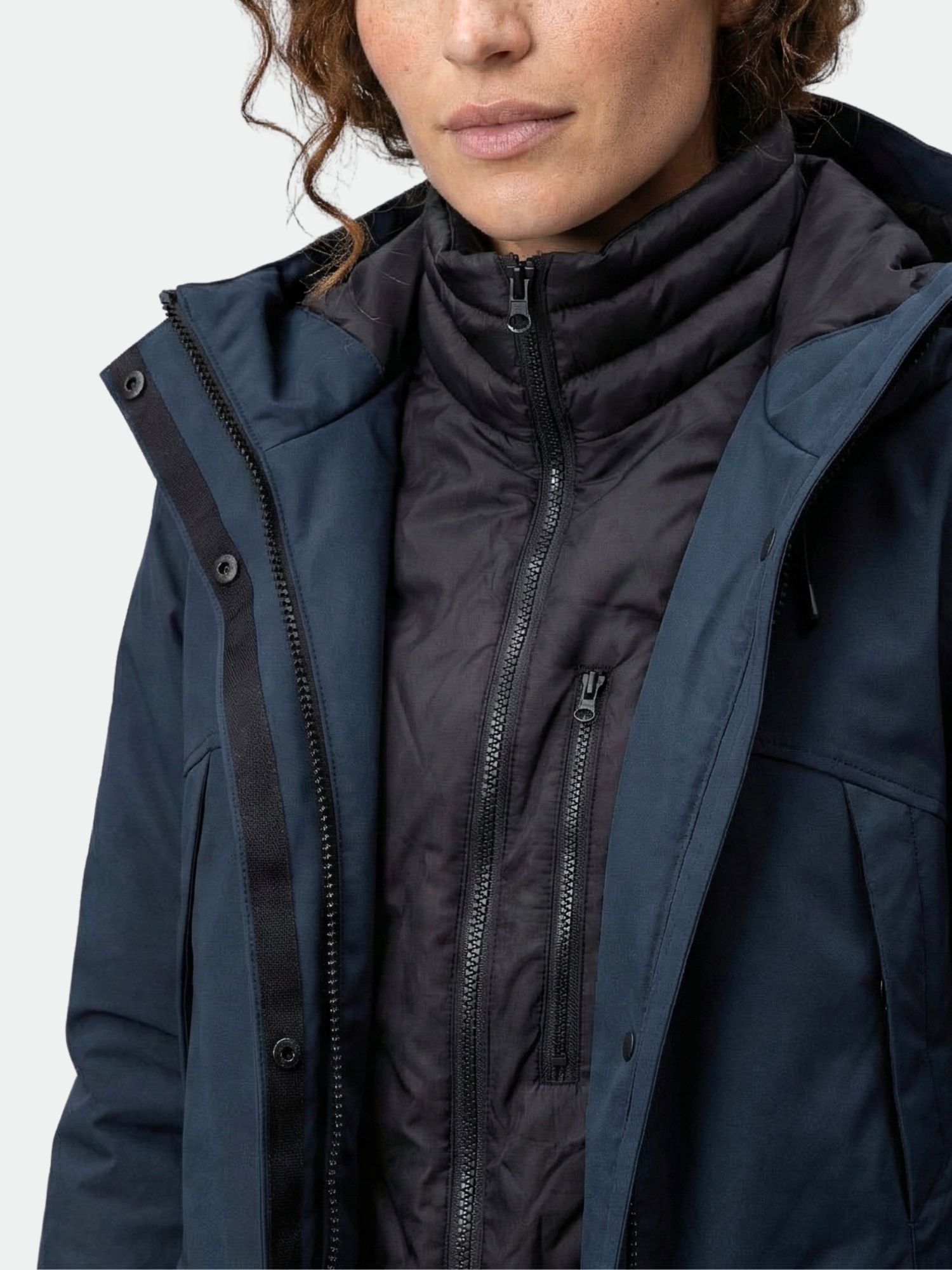 A woman models the Halti Bergga Women's DrymaxX Winter Parka in blue over a black zip-up puffer, shoulders up.