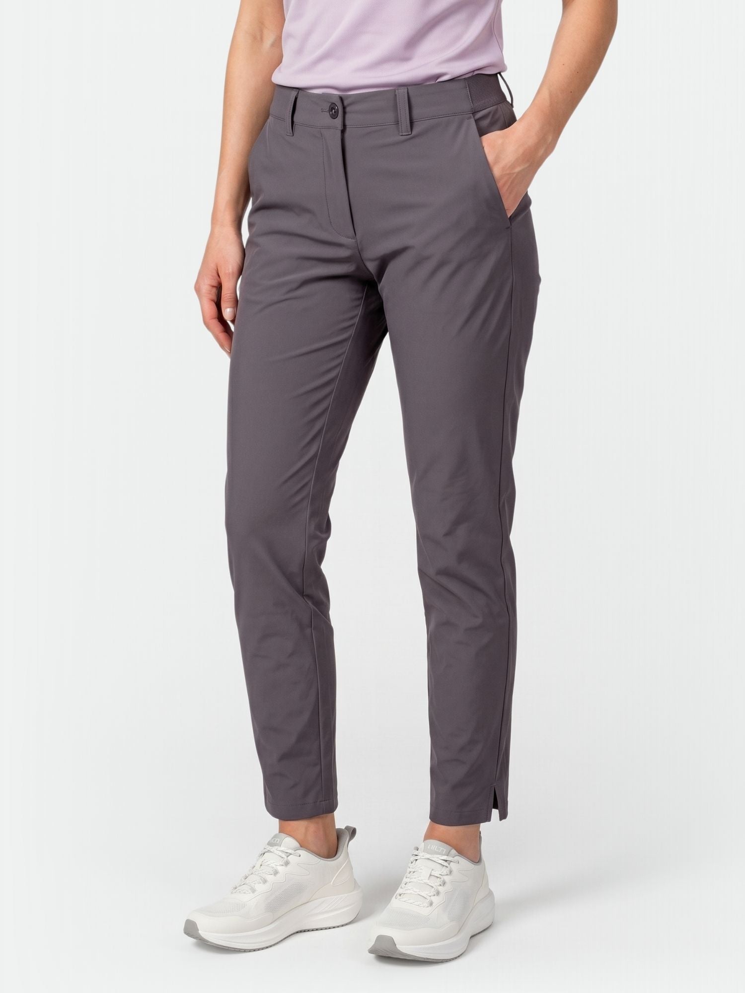 A woman in Halti Drive X-stretch Chinos, a light purple shirt, and white sneakers stands with one hand in her pocket.