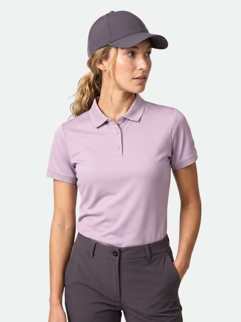 A woman in a Halti Laine Technical Polo Shirt made from breathable fabric stands with one hand in her pocket, looking aside.