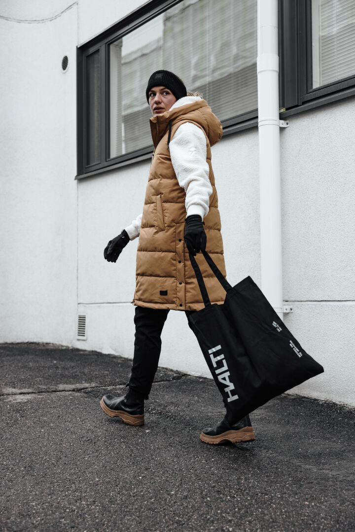 A person carries a black Halti bag over a Lykky Fleece Pullover Womens by Halti while outside in tan vest and boots.