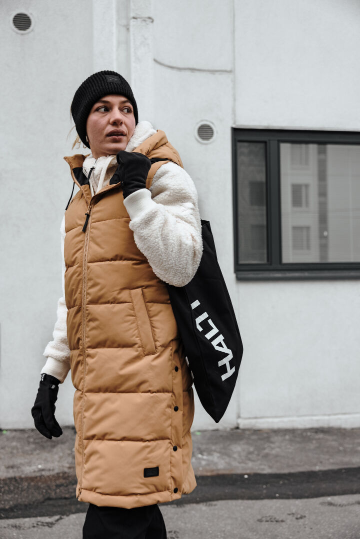 A woman in the Halti Lykky Fleece Pullover walks outside with a recycled tote near a white building.