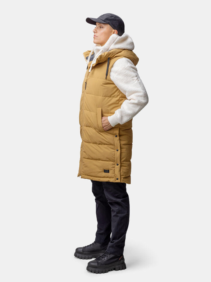 Woman in Halti Penger Puffer Vest, gray hoodie, and black cap stands in profile with hands in pockets.