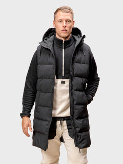 A man wears the Halti Penger Puffer Vest over a zip-up fleece and beige pants, standing facing forward.