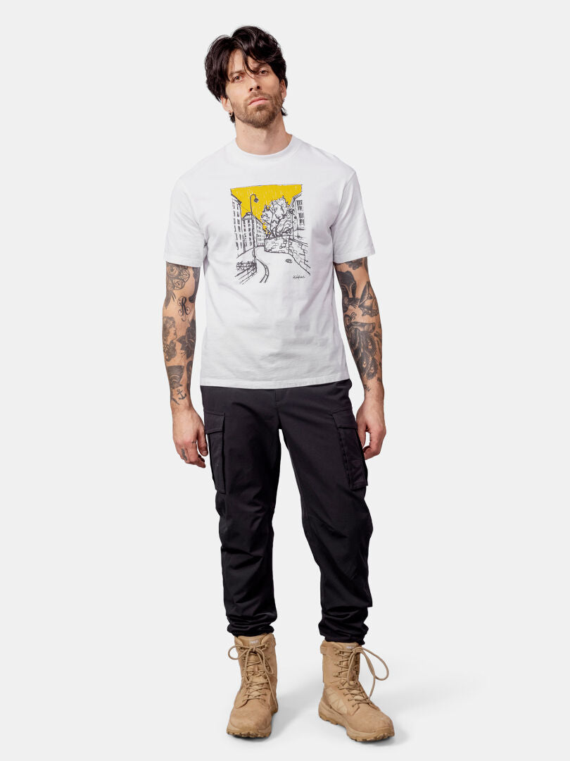 Man with tattoos in a Halti Skaltsi Unisex T-shirt, black cargo pants, and tan boots stands against a plain background.