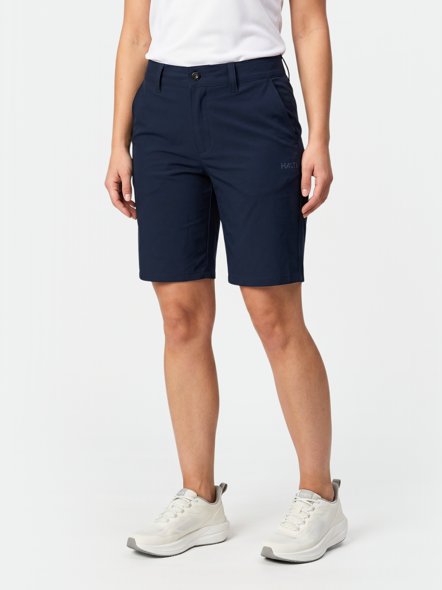 Wearing Halti Drive X-stretch Shorts for women, a white shirt, and sneakers, standing against a plain background.